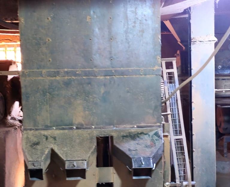 A tall separator in a dry mill, discharging graded coffee through a row of outlet chutes.