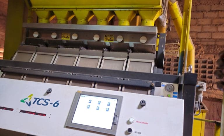 An optical colour sorter in operation, with feed chutes above the ejection chambers and a touchscreen control panel.