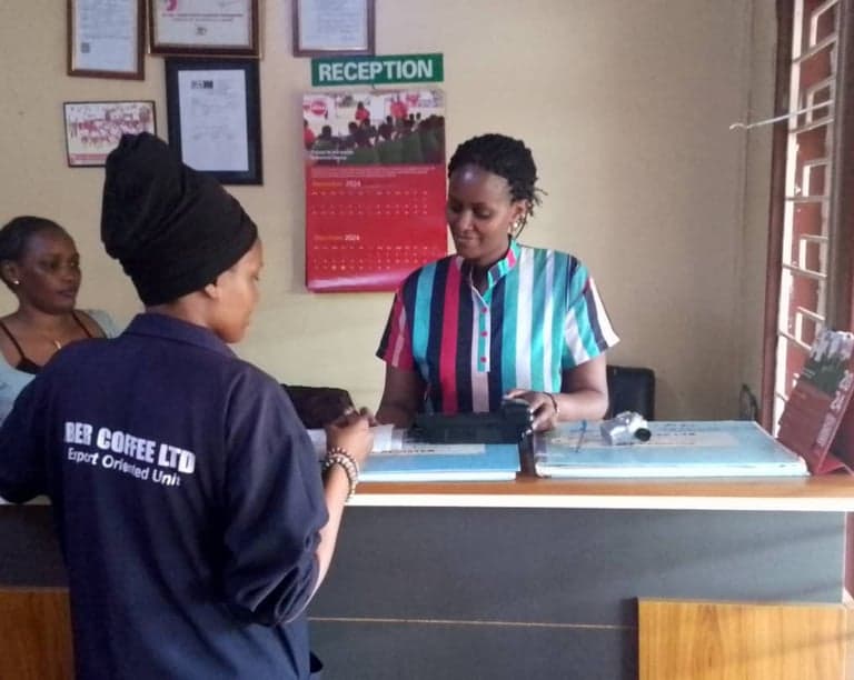 A worker in Jber Coffee Ltd Export Oriented Unit overalls at the reception counter, framed certificates on the wall behind.