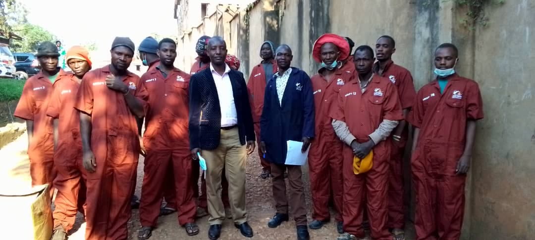 Warehouse and processing staff in numbered work overalls standing with two colleagues in office dress.